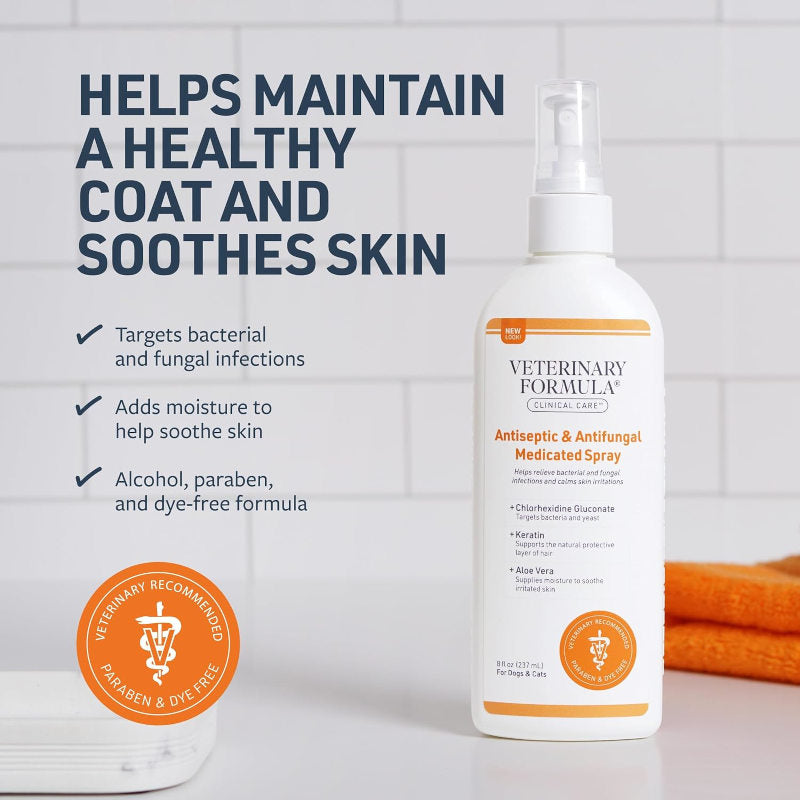 A bottle of Veterinary Formula Antiseptic & Antifungal Medicated Spray stands on a white surface against a white tiled wall. The bottle is white with orange accents and a white spray top.